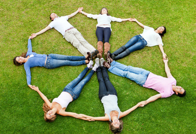 Circle of friends lying on the grass outdoors and smiling